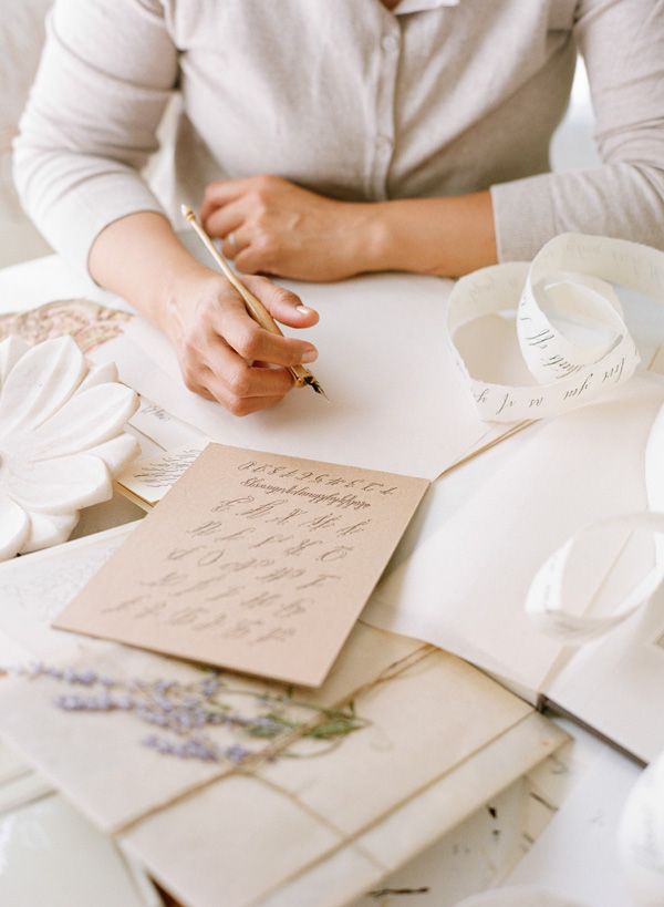 Hands writing calligraphy with a fountain pen at a desk of paper, ribbon and lavender