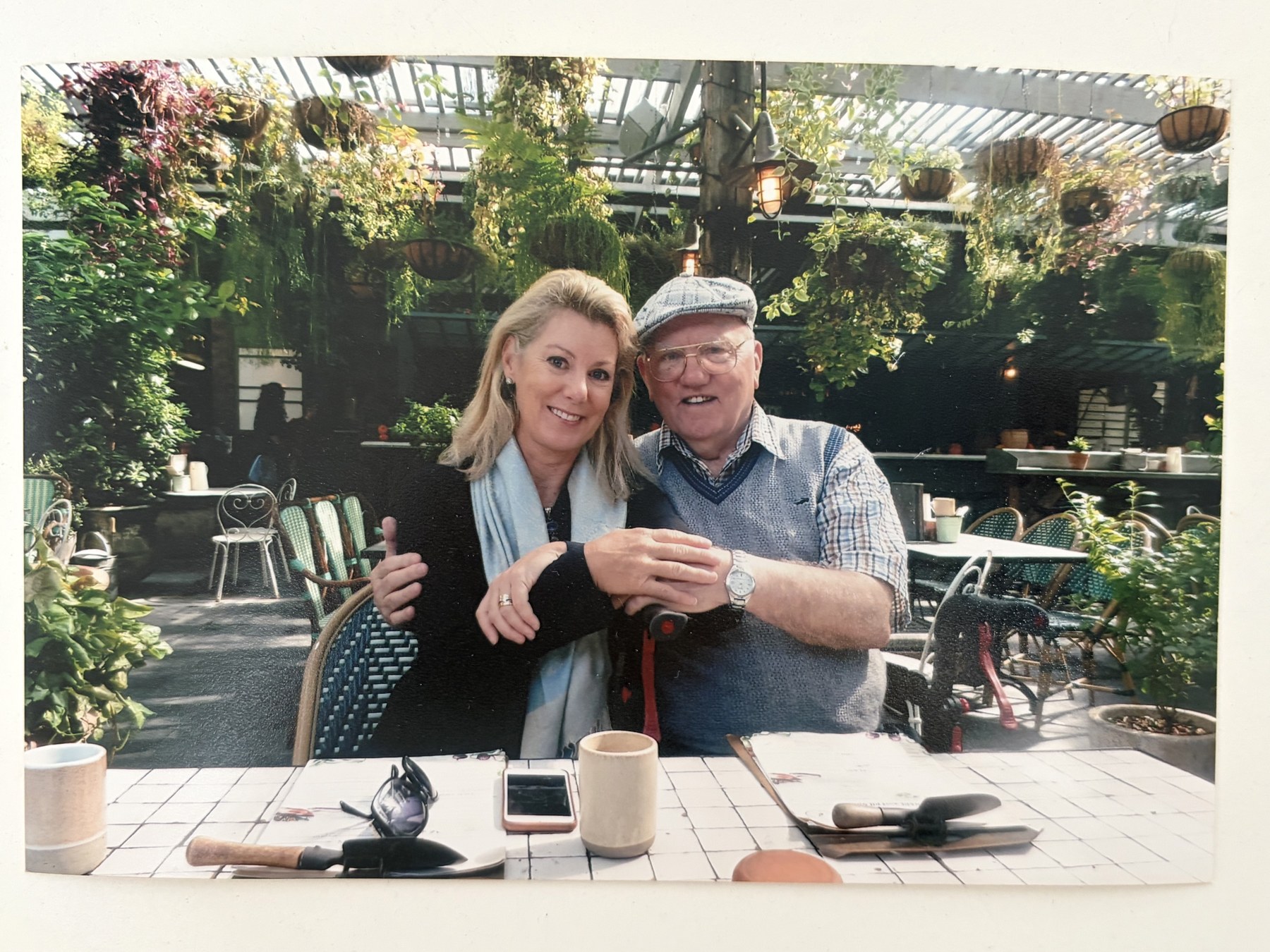 Kate with her father, sitting together at a plant-filled garden cafe